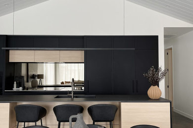 This is an example of a large contemporary galley eat-in kitchen in Hamilton with an undermount sink, flat-panel cabinets, black cabinets, solid surface benchtops, black splashback, mirror splashback, panelled appliances, concrete floors, with island, black floor, black benchtop and vaulted.