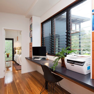 Photo of a small modern home office and library in Brisbane with white walls, medium hardwood flooring, a built-in desk and multi-coloured floors.