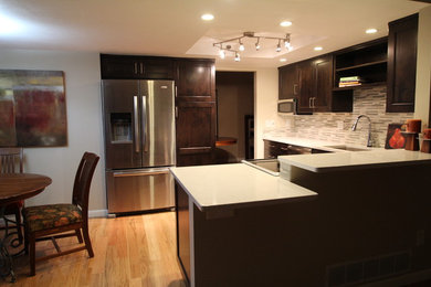Example of a small minimalist u-shaped light wood floor eat-in kitchen design in Denver with an undermount sink, shaker cabinets, dark wood cabinets, quartz countertops, white backsplash, mosaic tile backsplash, stainless steel appliances and a peninsula