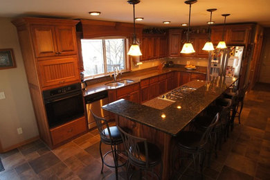 ミルウォーキーにあるトラディショナルスタイルのおしゃれなキッチン (ダブルシンク、落し込みパネル扉のキャビネット、中間色木目調キャビネット、御影石カウンター、シルバーの調理設備、スレートの床) の写真