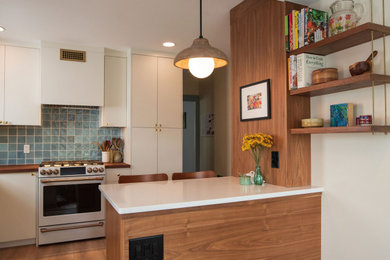 Example of a mid-sized mid-century modern u-shaped vinyl floor and brown floor enclosed kitchen design in Philadelphia with a double-bowl sink, flat-panel cabinets, medium tone wood cabinets, wood countertops, blue backsplash, porcelain backsplash, white appliances, a peninsula and brown countertops