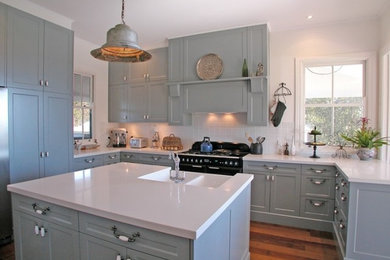 Inspiration for a traditional u-shaped kitchen in Sydney with a farmhouse sink, blue cabinets, white splashback, stainless steel appliances, recessed-panel cabinets, medium hardwood floors and with island.