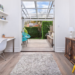 Skandinavisk inredning av ett litet hemmabibliotek, med vita väggar, ett fristående skrivbord, grått golv och laminatgolv