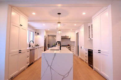 Open concept kitchen - large contemporary galley light wood floor and beige floor open concept kitchen idea in Other with an undermount sink, shaker cabinets, white cabinets, quartz countertops, white backsplash, marble backsplash, stainless steel appliances and an island