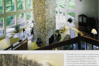 Diseño de sala de estar abierta actual grande con paredes blancas, suelo de madera clara, chimenea de doble cara, marco de chimenea de piedra y suelo amarillo