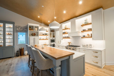 Open concept kitchen - large modern l-shaped light wood floor and beige floor open concept kitchen idea in Cleveland with a farmhouse sink, shaker cabinets, white cabinets, marble countertops, white backsplash, stainless steel appliances, an island and white countertops