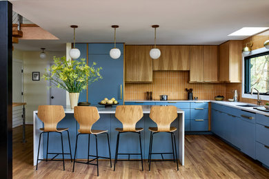 Example of a 1960s u-shaped medium tone wood floor and brown floor kitchen design in DC Metro with an undermount sink, flat-panel cabinets, blue cabinets, orange backsplash, paneled appliances, an island and white countertops