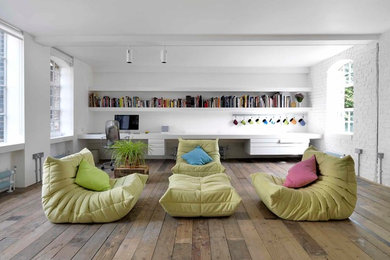 Design ideas for an industrial open concept living room in London with a library, white walls and medium hardwood floors.