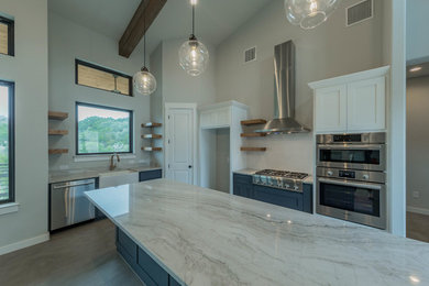 This is an example of a modern u-shaped open plan kitchen in Austin with a farmhouse sink, flat-panel cabinets, blue cabinets, marble benchtops, stainless steel appliances, ceramic floors, with island, grey floor and multi-coloured benchtop.
