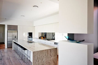 Photo of a large modern single-wall kitchen pantry in Melbourne with an undermount sink, recessed-panel cabinets, white cabinets, terrazzo benchtops, metallic splashback, glass sheet splashback, stainless steel appliances, painted wood floors, with island, brown floor and beige benchtop.
