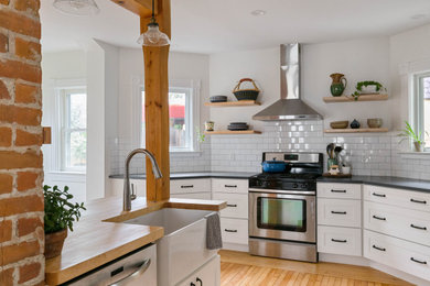 Inspiration for a mid-sized contemporary kitchen in Burlington with a farmhouse sink, shaker cabinets, white cabinets, quartz benchtops, white splashback, ceramic splashback, stainless steel appliances, light hardwood floors, with island, grey benchtop and exposed beam.