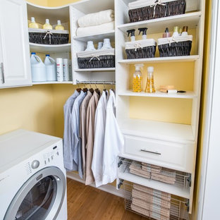 Inspiration for a medium sized l-shaped utility room in Cincinnati with raised-panel cabinets, white cabinets, yellow walls, bamboo flooring and a side by side washer and dryer.