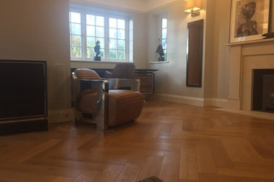 Expansive contemporary enclosed living room in Sussex with grey walls, medium hardwood floors, a wood stove and a stone fireplace surround.