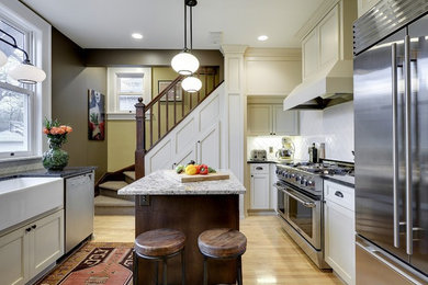 Enclosed kitchen - small transitional l-shaped light wood floor enclosed kitchen idea in Minneapolis with a farmhouse sink, recessed-panel cabinets, white cabinets, granite countertops, white backsplash, porcelain backsplash, stainless steel appliances and an island