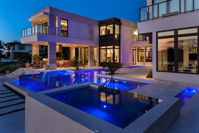 Large modern backyard custom-shaped infinity pool in Miami with natural stone pavers and a hot tub.
