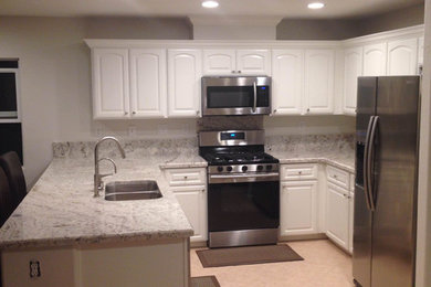 Example of a mid-sized classic u-shaped porcelain tile and white floor enclosed kitchen design in San Diego with a double-bowl sink, raised-panel cabinets, white cabinets, granite countertops, gray backsplash, stone slab backsplash, stainless steel appliances and a peninsula