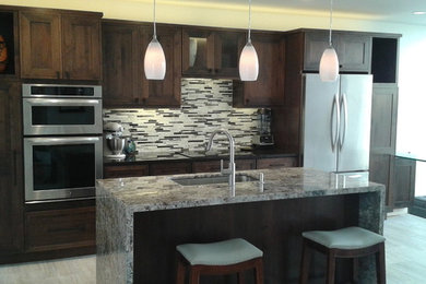 Inspiration for a mid-sized transitional single-wall light wood floor eat-in kitchen remodel in Los Angeles with an undermount sink, shaker cabinets, brown cabinets, granite countertops, multicolored backsplash, mosaic tile backsplash, stainless steel appliances, an island and multicolored countertops