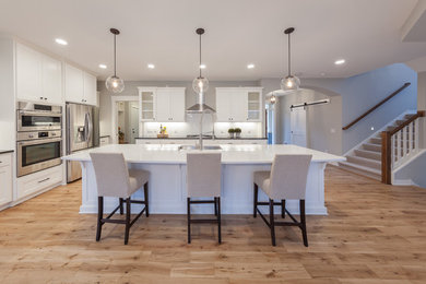 Mid-sized country galley eat-in kitchen in Minneapolis with an undermount sink, shaker cabinets, white cabinets, quartz benchtops, white splashback, porcelain splashback, stainless steel appliances, medium hardwood floors, with island and brown floor.