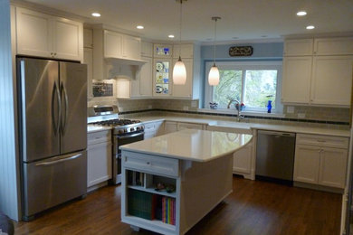 Example of a mid-sized farmhouse l-shaped medium tone wood floor eat-in kitchen design in Chicago with a farmhouse sink, recessed-panel cabinets, white cabinets, quartz countertops, gray backsplash, ceramic backsplash, stainless steel appliances and an island