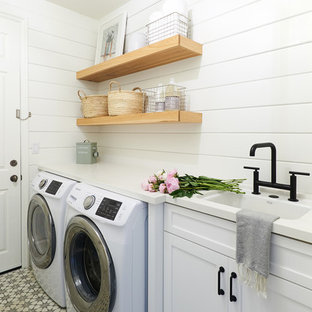 Modelo de cuarto de lavado lineal, costero, con fregadero bajoencimera, armarios estilo shaker, puertas de armario blancas, paredes blancas, lavadora y secadora juntas, suelo multicolor y encimeras blancas