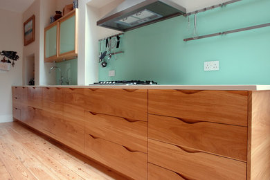 Large contemporary galley separate kitchen in London with an undermount sink, flat-panel cabinets, medium wood cabinets, quartz benchtops, green splashback, glass sheet splashback, stainless steel appliances, light hardwood floors and with island.
