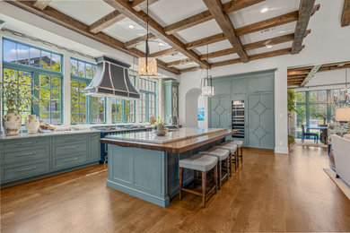 Example of a huge classic l-shaped medium tone wood floor, brown floor and exposed beam open concept kitchen design in Dallas with an undermount sink, recessed-panel cabinets, blue cabinets, granite countertops, multicolored backsplash, ceramic backsplash, black appliances, an island and gray countertops