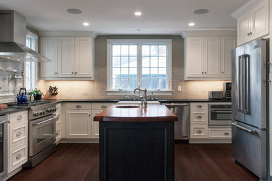 Example of a large classic l-shaped dark wood floor open concept kitchen design in DC Metro with a farmhouse sink, recessed-panel cabinets, white cabinets, beige backsplash, subway tile backsplash, stainless steel appliances and an island