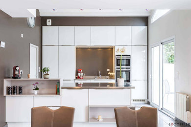 Photo of a medium sized contemporary galley open plan kitchen in Lyon with an integrated sink, flat-panel cabinets, white cabinets, stainless steel worktops, metallic splashback, stainless steel appliances, ceramic flooring, a breakfast bar, grey floors and grey worktops.