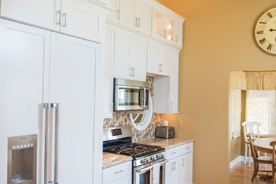 Example of a large beach style galley light wood floor eat-in kitchen design in Philadelphia with a double-bowl sink, shaker cabinets, white cabinets, granite countertops, brown backsplash, glass tile backsplash, stainless steel appliances and no island