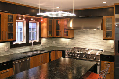This is an example of a mid-sized transitional l-shaped kitchen in Denver with an undermount sink, glass-front cabinets, medium wood cabinets, grey splashback, mosaic tile splashback, stainless steel appliances, with island, black benchtop and soapstone benchtops.