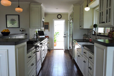 Eat-in kitchen - coastal galley medium tone wood floor eat-in kitchen idea in Santa Barbara with no island, recessed-panel cabinets, white cabinets, granite countertops, gray backsplash, mosaic tile backsplash, stainless steel appliances and a farmhouse sink