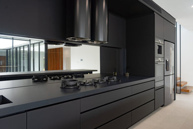 Ejemplo de cocina industrial grande con puertas de armario negras, encimera de cuarzo compacto, salpicadero con efecto espejo, una isla y encimeras grises