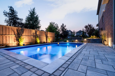 Example of a mid-sized transitional backyard concrete paver and rectangular pool landscaping design in Other