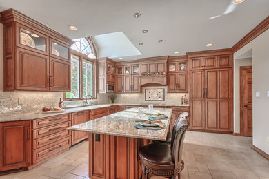 Inspiration for a large timeless l-shaped porcelain tile eat-in kitchen remodel in St Louis with an undermount sink, raised-panel cabinets, medium tone wood cabinets, beige backsplash, stone tile backsplash, paneled appliances and an island