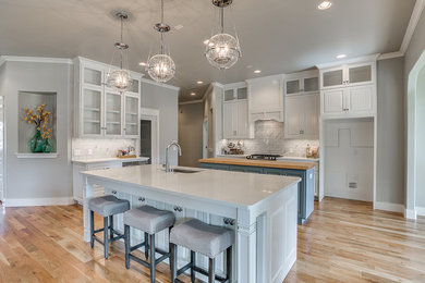 Example of a mid-sized transitional l-shaped dark wood floor and brown floor open concept kitchen design in Oklahoma City with a farmhouse sink, shaker cabinets, gray cabinets, quartz countertops, multicolored backsplash, stone tile backsplash, stainless steel appliances and an island