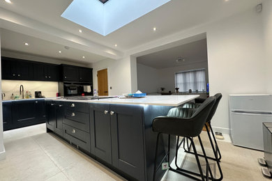 Large contemporary kitchen in Cheshire with a double-bowl sink, shaker cabinets, blue cabinets, quartz worktops, black appliances, porcelain flooring, an island, beige floors and white worktops.