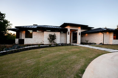 Photo of a large contemporary two-storey white house exterior in Dallas with stone veneer, a clipped gable roof and a metal roof.
