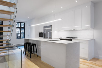 Small contemporary single-wall open plan kitchen in Montreal with an undermount sink, flat-panel cabinets, white cabinets, quartz benchtops, white splashback, ceramic splashback, stainless steel appliances, light hardwood floors and with island.