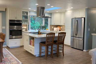 他の地域にある高級な中くらいなトラディショナルスタイルのおしゃれなキッチン (アンダーカウンターシンク、レイズドパネル扉のキャビネット、白いキャビネット、クオーツストーンカウンター、茶色いキッチンパネル、サブウェイタイルのキッチンパネル、シルバーの調理設備、ラミネートの床、茶色い床、白いキッチンカウンター) の写真