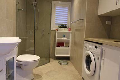 Photo of a modern bathroom in Sydney with flat-panel cabinets, white cabinets, a corner shower, a two-piece toilet, beige tile, an integrated sink and a hinged shower door.