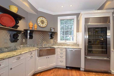 Mid-sized trendy l-shaped medium tone wood floor enclosed kitchen photo in Philadelphia with a farmhouse sink, beaded inset cabinets, beige cabinets, granite countertops, metallic backsplash, stainless steel appliances and a peninsula