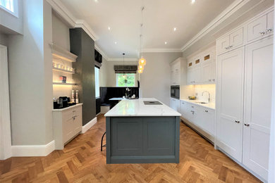 This is an example of a large classic grey and white u-shaped open plan kitchen in Other with a single-bowl sink, shaker cabinets, medium wood cabinets, composite countertops, white splashback, engineered quartz splashback, black appliances, medium hardwood flooring, an island, white worktops and feature lighting.