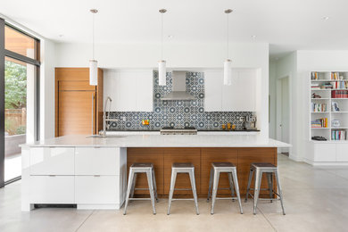 Open concept kitchen - mid-century modern beige floor open concept kitchen idea in Denver with an undermount sink, flat-panel cabinets, white cabinets, multicolored backsplash, paneled appliances, an island and black countertops