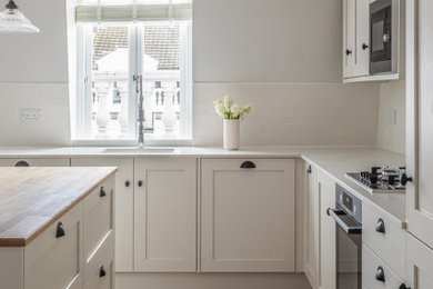 ロンドンにあるお手頃価格の中くらいなトランジショナルスタイルのおしゃれなキッチン (アンダーカウンターシンク、シェーカースタイル扉のキャビネット、白いキャビネット、珪岩カウンター、白いキッチンパネル、磁器タイルのキッチンパネル、パネルと同色の調理設備、淡色無垢フローリング、茶色い床、白いキッチンカウンター) の写真