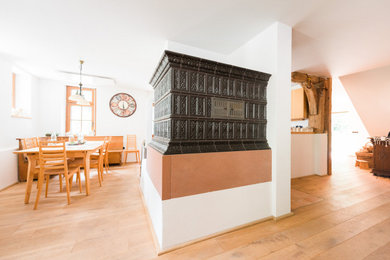 Rustikales Wohnzimmer mit weißer Wandfarbe, hellem Holzboden, Kaminofen und gefliester Kaminumrandung in Sonstige