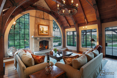 Mid-sized farmhouse loft-style medium tone wood floor and brown floor living room library photo in Santa Barbara with beige walls, a standard fireplace, a stone fireplace and a concealed tv
