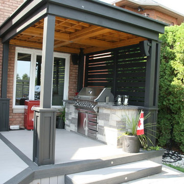 A large low maintenance deck with a BBQ area with a shade roof over it.