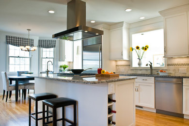 Example of a mid-sized transitional u-shaped light wood floor and brown floor open concept kitchen design in Boston with an undermount sink, shaker cabinets, white cabinets, granite countertops, beige backsplash, ceramic backsplash, stainless steel appliances and an island
