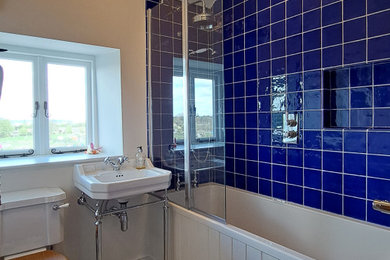 This is an example of a small traditional bathroom in Oxfordshire with a built-in bath, a shower/bath combination, a two-piece toilet, blue tiles, ceramic tiles, porcelain flooring, blue floors, a single sink and a freestanding vanity unit.