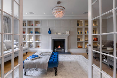 Inspiration for a large transitional formal enclosed living room in London with grey walls, medium hardwood floors, no tv, a standard fireplace and brown floor.